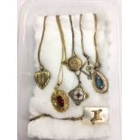 Seven pendants and lockets on chains.