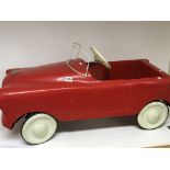 A Vintage Tri-ang pedal car, painted red with white wheels.