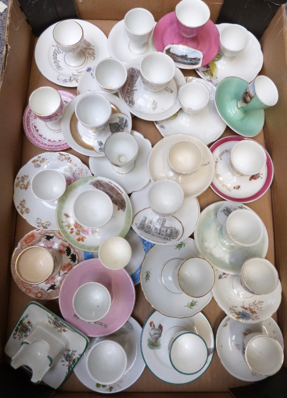 Approximately 28 novelty egg cups with saucers including floral decorated, souvenir ware etc