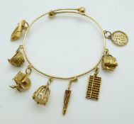 Chinese 20k gold bangle with eight 20k gold charms by Luen Wo including a teapot, abacus, parasol,