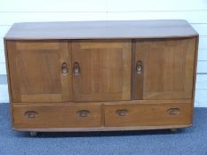 Ercol light elm sideboard with three cupboard doors over two drawers raised on castors with