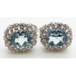 A pair of 9ct white gold earrings each set with an oval cut aquamarine surrounded by diamonds