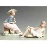 Two Nao figurines, one holding a parasol with baskets of flowers, the other a reclining ballerina,