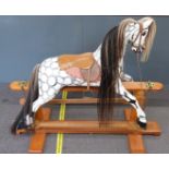 A wooden dapple grey rocking horse with hair mane and tail, leather saddle and reins, metal mounts