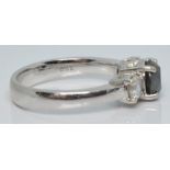 An 18ct white gold ring set with a round cut black diamond flanked by two diamonds, each