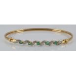 A 9ct gold bangle set with emeralds and diamonds, 4.9g