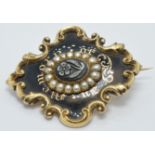 A Victorian enamel mourning brooch set with a flower plaque, black enamel and seed pearls reading '