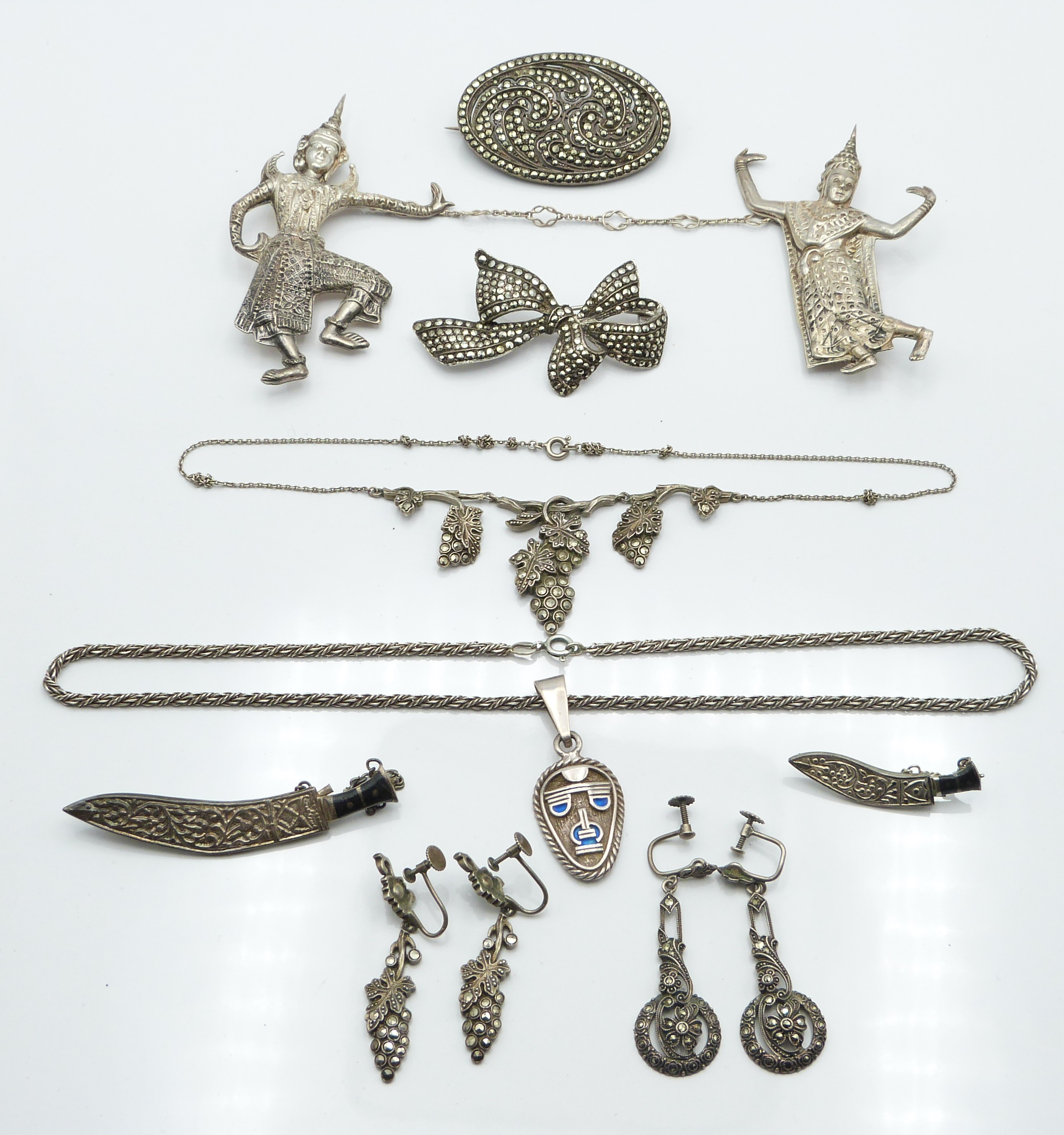 Two Siam silver brooches depicting deities, a silver pendant depicting a mask, white metal knife
