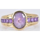 A 9ct gold ring set with an oval cut amethyst and four further round cut amethysts to each shoulder,