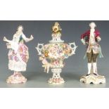 A pair of Dresden lace figures and a covered pedestal vase with applied flower decoration,