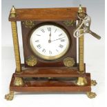 French brass mantel clock mounted on mahogany frame with brass pillar supports, raised on paw