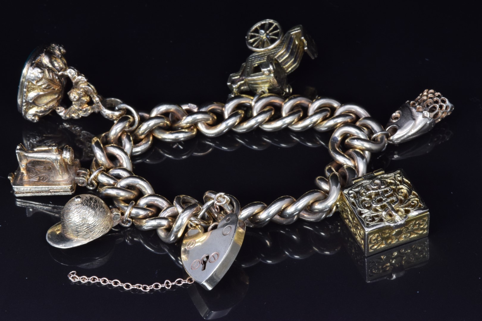 A 9ct gold charm bracelet with five 9ct gold charms including sewing machine, fob, jockey's hat