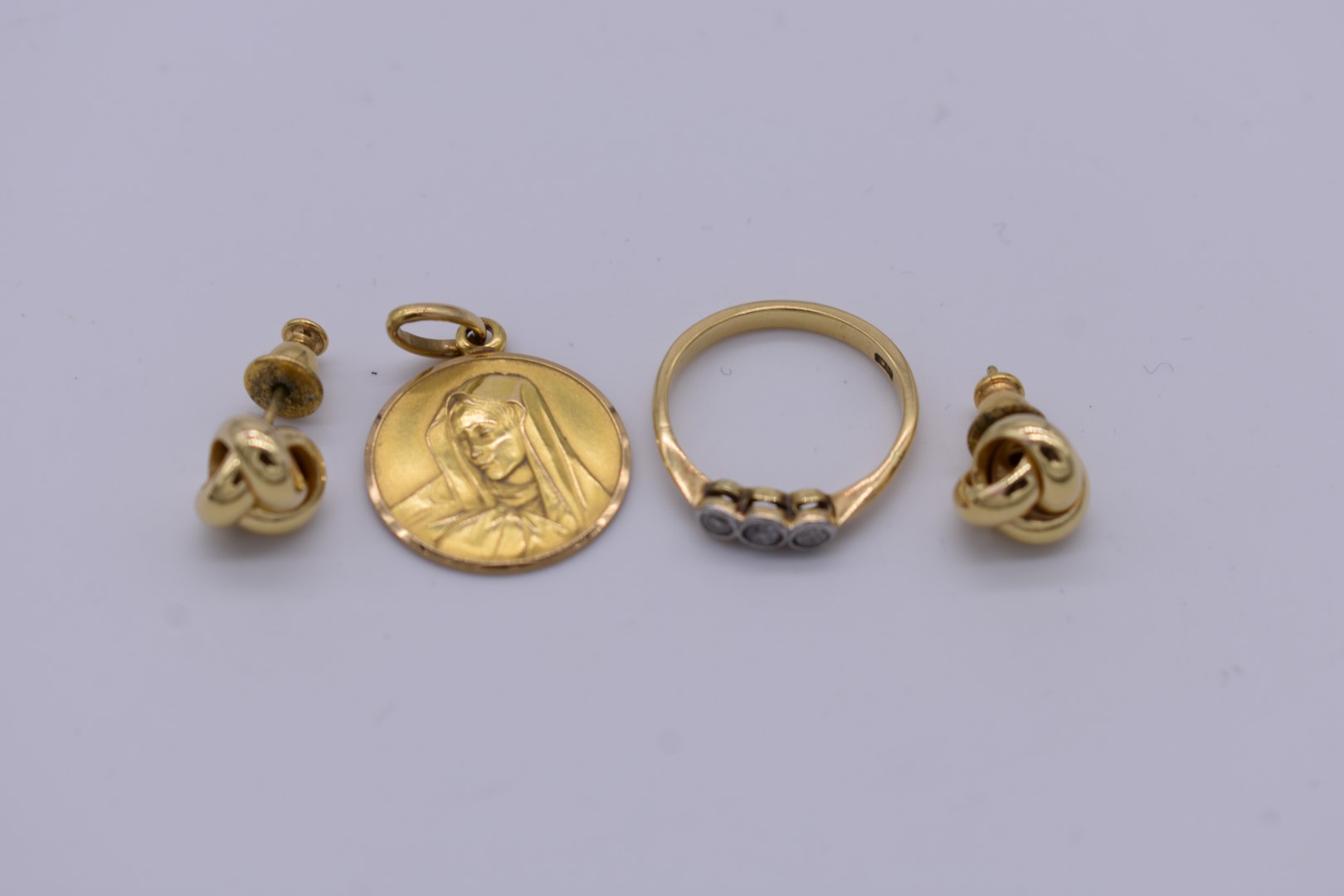A triple diamond gold ring; together with a pair of gold knot ear studs; and a gold Madonna