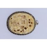 A Chinese carved ivory and white metal mounted oval pendant, the ivory 4 x 3cm.