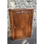 A George III oak and crossbanded mahogany hanging corner cupboard, the door enclosing shaped