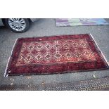 A Persian rug, having repeated design to central field, with geometric borders on a red ground,
