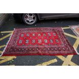 An old Bokhara style rug, having twelve medallions to central field on a red ground, 190 x 130cm.