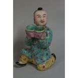 A Chinese famille rose kneeling boy, painted mark to base, 16.5cm high, (repaired).