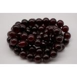 A string of spherical cherry amber beads, 84cm, 97.5g.