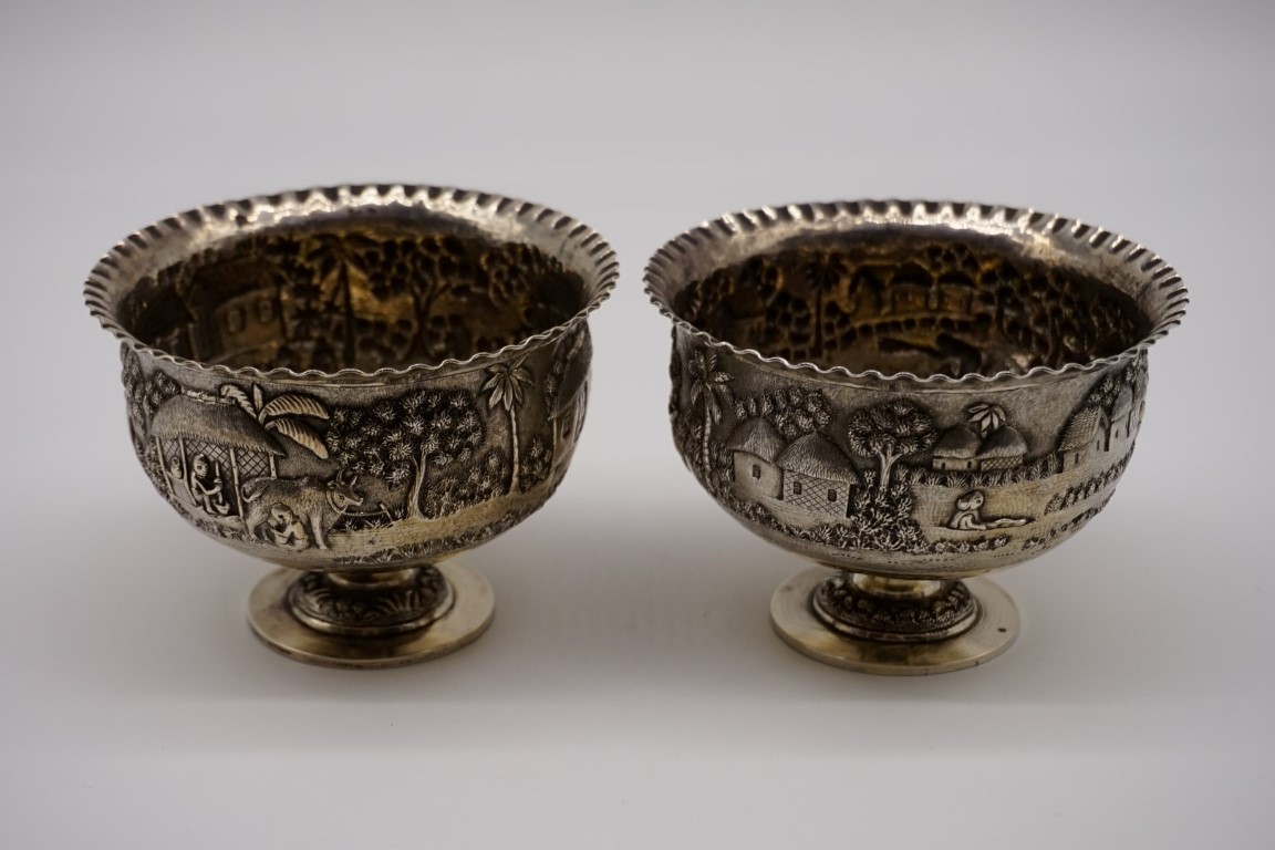 A pair of Indian white metal pedestal bowls, decorated village scenes, 8.5cm high. - Image 2 of 3