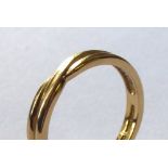AN 18CT GOLD WEDDING BAND In a half twist form (size L).