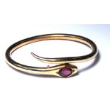 A VINTAGE YELLOW METAL AND GARNET SNAKE BRACELET The single oval cut stone in plain mount, in a