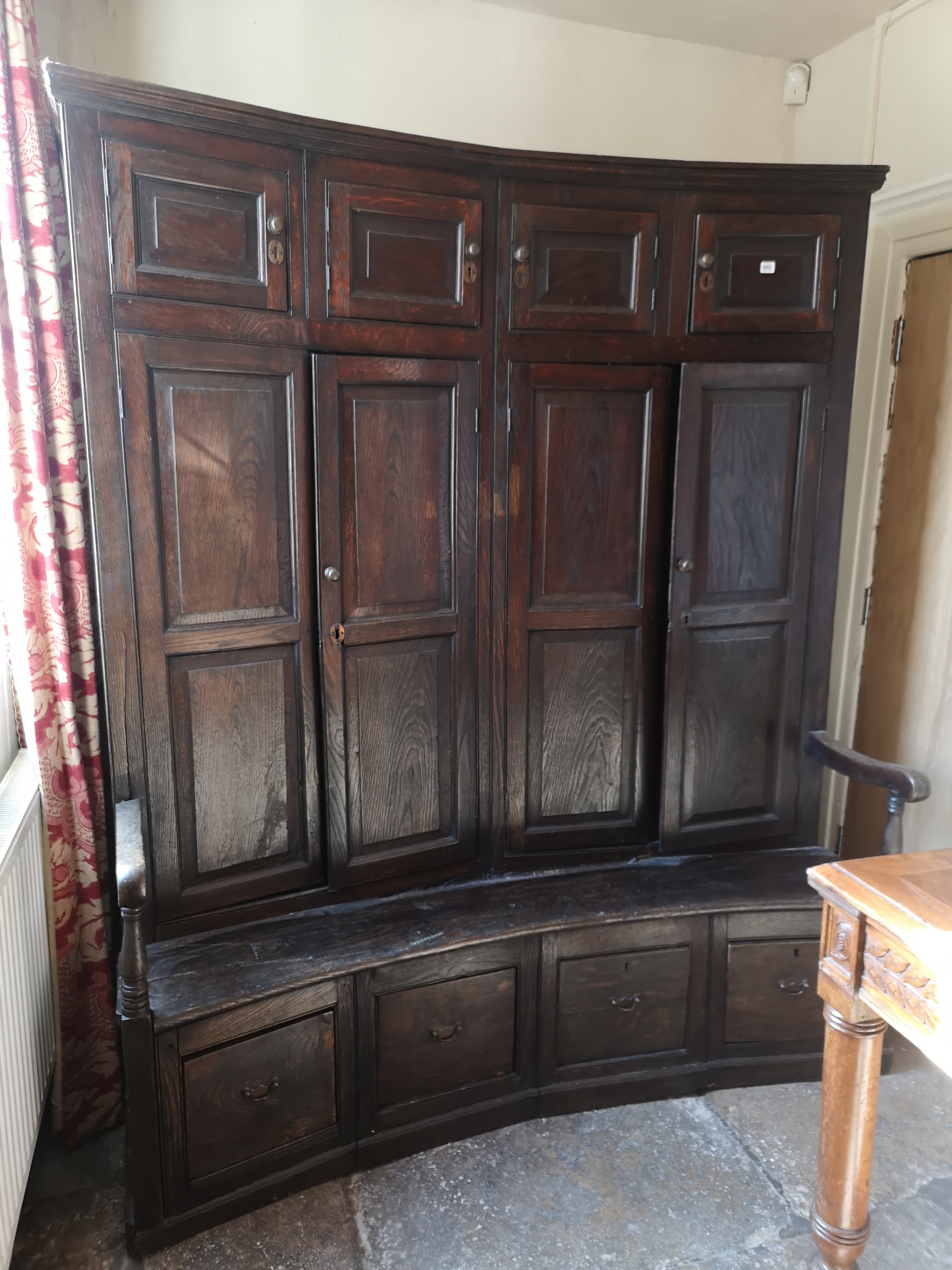 AN ANTIQUE OAK BACON SETTLE The concave back with fielded panelled cupboards above solid seat and