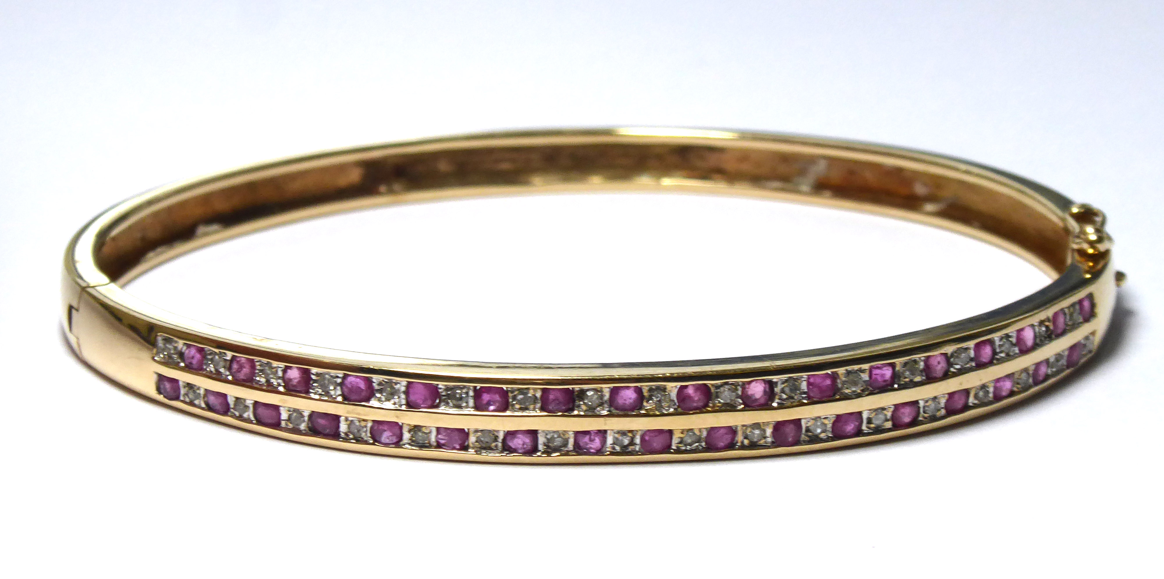 A VINTAGE YELLOW METAL, DIAMOND AND RUBY BANGLE Two rows of oval cut rubies interspersed with