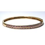 A VINTAGE YELLOW METAL, DIAMOND AND RUBY BANGLE Two rows of oval cut rubies interspersed with