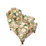 AN EARLY 20TH CENTURY CLUB ARMCHAIR In a floral upholstery on a green ground, on squat mahogany