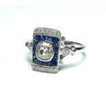 AN ART DECO DESIGN RING Set with a central old cut .77 diamond surrounded by sapphires and diamonds,