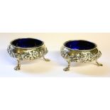 A PAIR OF GEORGE II SILVER AND BLUE GLASS SALTS Having embossed decoration and tripod legs,