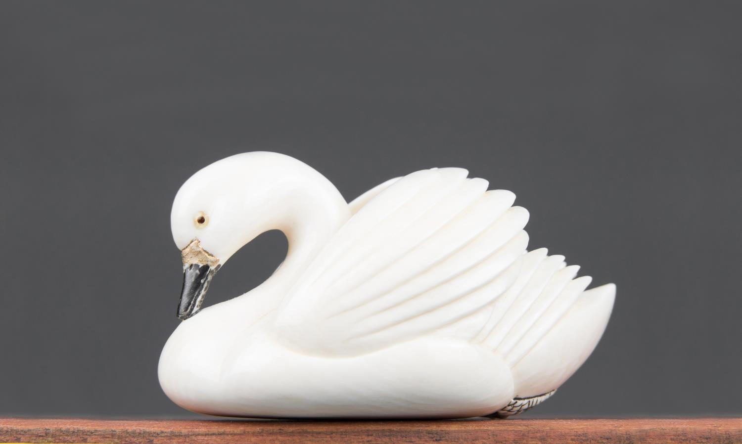 AN EARLY 20TH CENTURY JAPANESE NETSUKE IVORY CARVING OF A GLIDING SWAN, WITH INLAID EYES AND BLACK