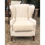 A 20TH CENTURY WING ARMCHAIR Newly upholstered in a cream fabric with red piping, raised on square