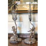 A PAIR OF EARLY 20TH CENTURY TABLE LAMPS Figured with silvered bronze prancing winged cherubs, on