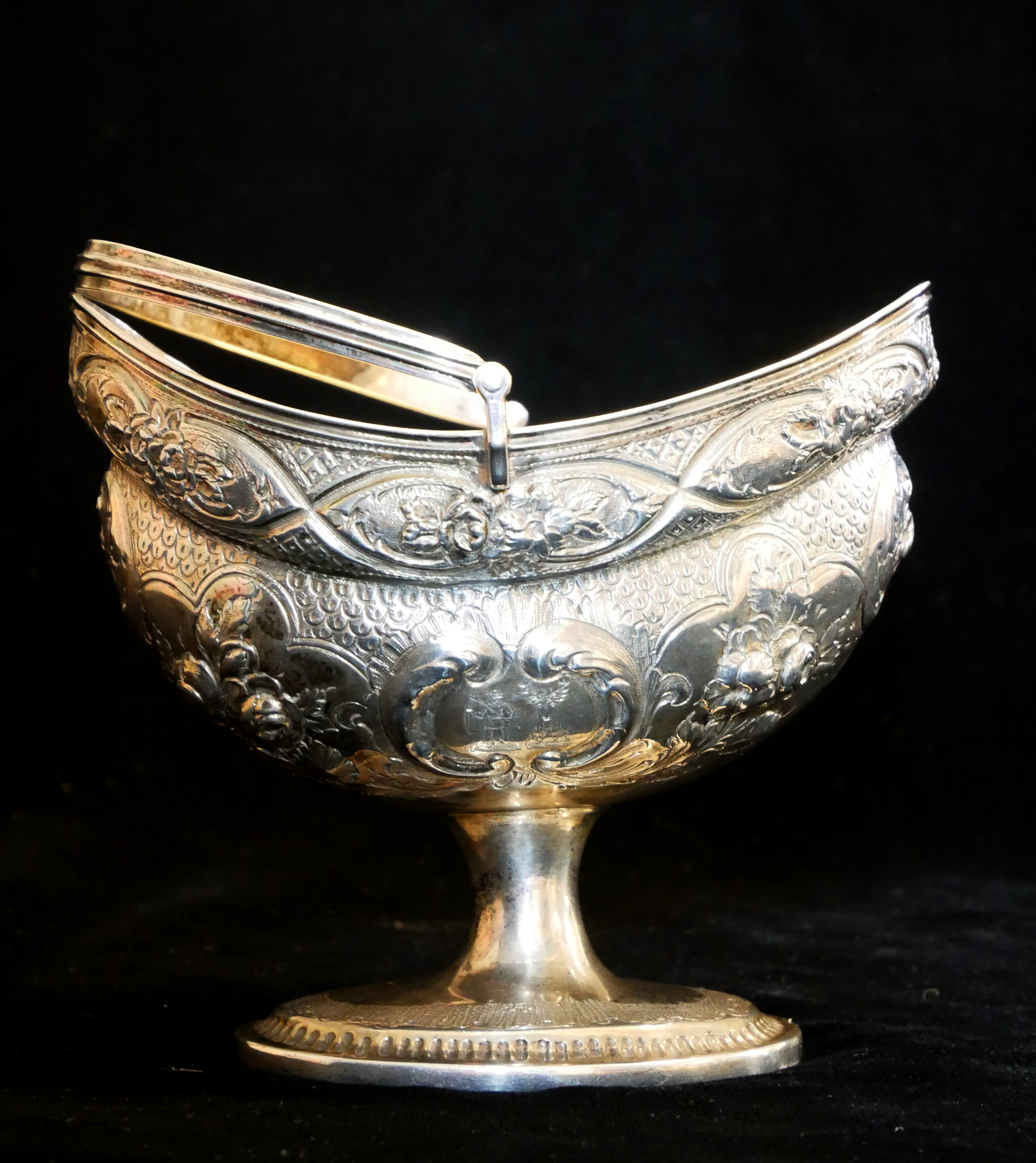 A GEORGIAN IRISH SILVER SWEETMEAT BASKET Having a swing handle, embossed floral decoration and