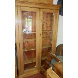 A FLOORSTANDING STAINED PINE GLAZED BOOKSHELF With adjustable shelves, raised on plinth base. (114cm