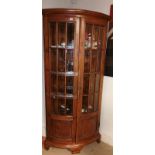 A HARDWOOD BOW FRONT FLOORSTANDING CORNER CABINET With glazed and panned doors, raised on bracket