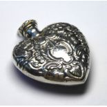 A WHITE METAL HEART FORM SCENT BOTTLE Embossed scrolled decoration and spatula cap. (tests as