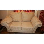 A TWO SEATER SCROLL END SOFA In cream floral fabric upholstery, with loose cushions. (165cm x 90cm x