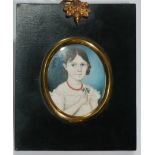 A 19TH CENTURY OVAL MINIATURE NAIVE SHOOL PORTRAIT Young lady wearing a coral necklace and holding a