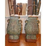 A PAIR OF CHINESE ARCHAIC DESIGN BRONZE LAMPS Having twin dragon form loop handles and verdigris