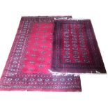 TWO AFGHAN WOOLLEN RUGS Of traditional design on a red ground. (142cm x 207cm) (98cm x 157cm)