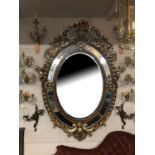 A LARGE ITALIAN INSPIRED OVAL PARCEL GILT BEVELLED EDGE MIRROR Profusely decorated with foliage