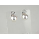 A PAIR OF 18CT WHITE GOLD AND SOUTH SEA ISLAND PEARL AND DIAMOND DROP EARRINGS The single pearl with