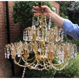 A GILT METAL TWELVE BRANCH CHANDELIER FESTOONED WITH CRYSTAL DROPS.