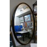 A LARGE OVAL BEVELLED EDGE MIRROR With ebonised and parcel gilt frame. (107cm x 187cm)