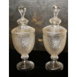 A PAIR OF REGENCY STYLE CUT GLASS URNS AND COVERS With faceted finials above faux hobnail bodies. (