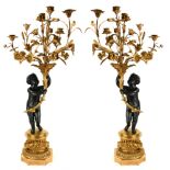 A LARGE PAIR OF GILT AND PATINATED BRONZE SIX SCONCE CANDELABRA IN THE FORM OF PUTTI Holding foliage