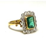 AN 18CT GOLD, EMERALD AND DIAMOND CLUSTER RING Having a trap cut emerald, edged with round cut